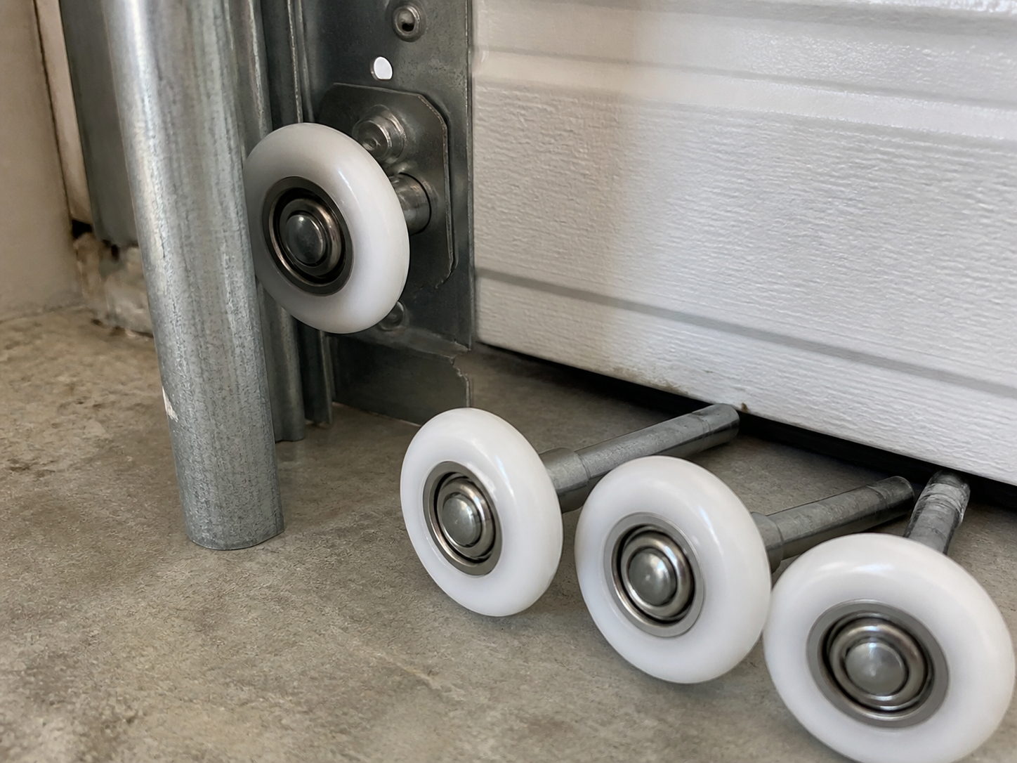 White nylon garage door rollers beside a roller installed in residential garage door hardware